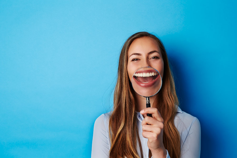 young woman in front of blue background smiling into magnifying glass