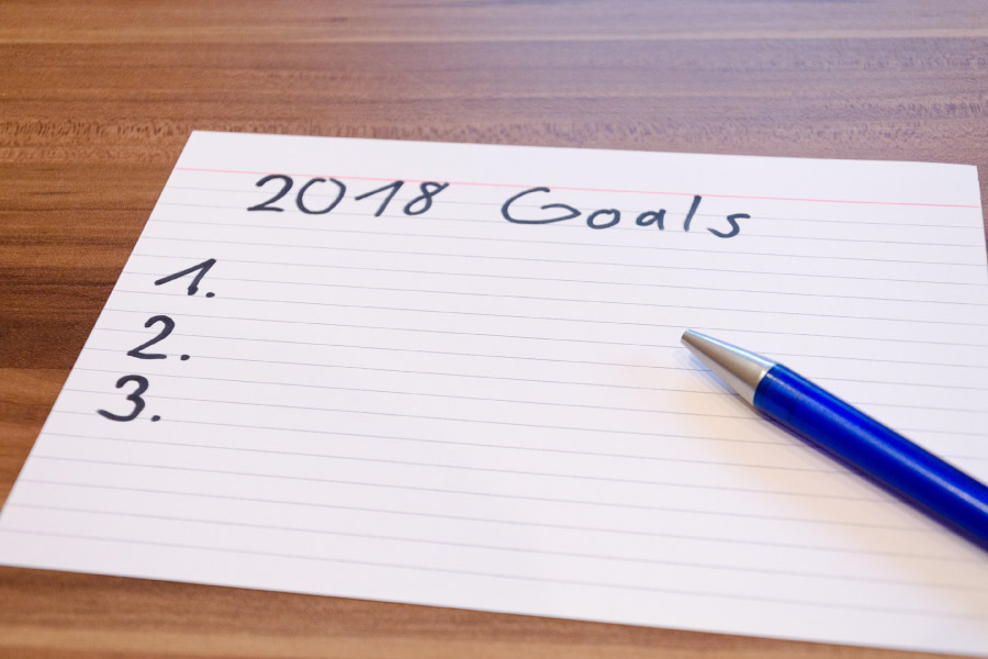 Lined notecard labeled 2018 Goals and numbered one, two, and three with a blue pen on top of the paper.