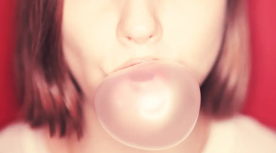 Woman with red hair blows a large pink gum bubble