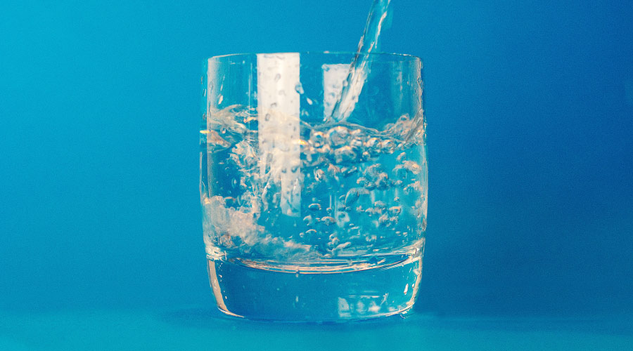 Clear glass with water containing cavity-fighting fluoride being poured into it against a sky blue background