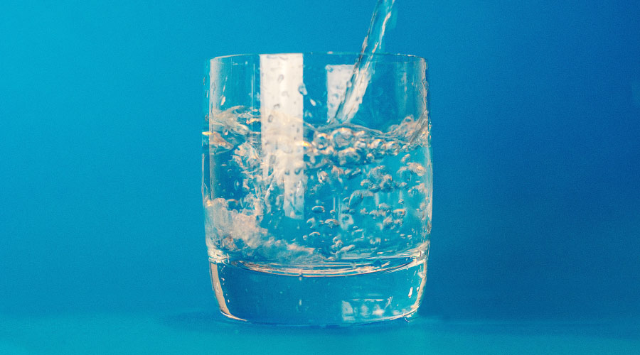 Glas waarin water met het gaatjesbestrijdende fluoride wordt gegoten tegen een hemelsblauwe achtergrond