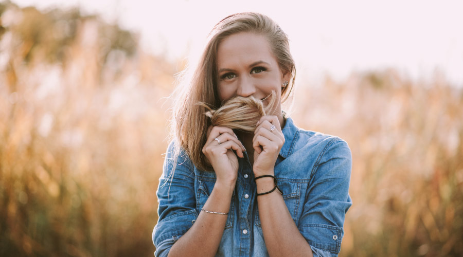 Blonde young woman wearing a denim shirt covers her mouth with her hair because she's embarrassed about her tonsil stones