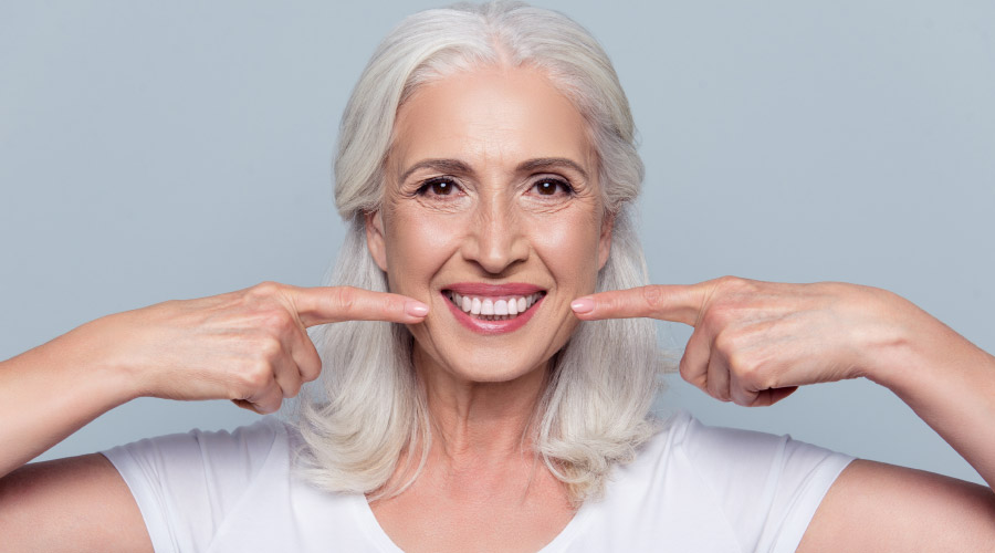 woman with long white hair pointing at her white, stain-free teeth with both forefingers