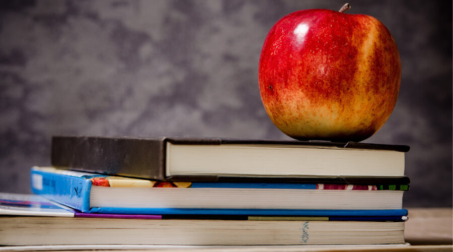 apple sitting on top of three school books