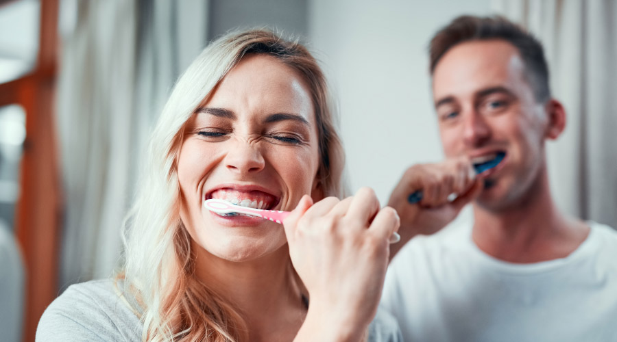 Woman & man in the background brushing their teeth to eliminate the risk of cavities