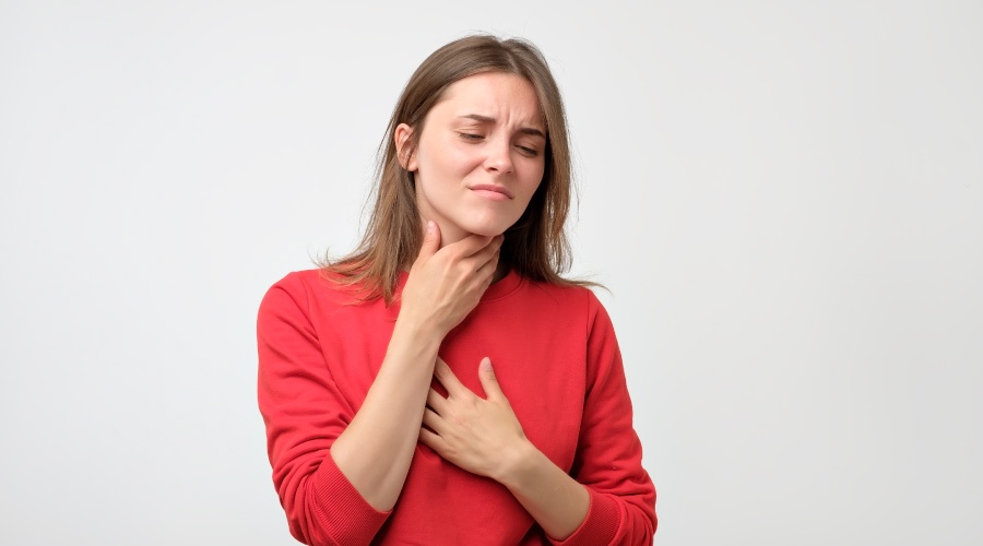 Woman in red sweater holding her throat with her eyes closed and face looking pained because of tonsil stones