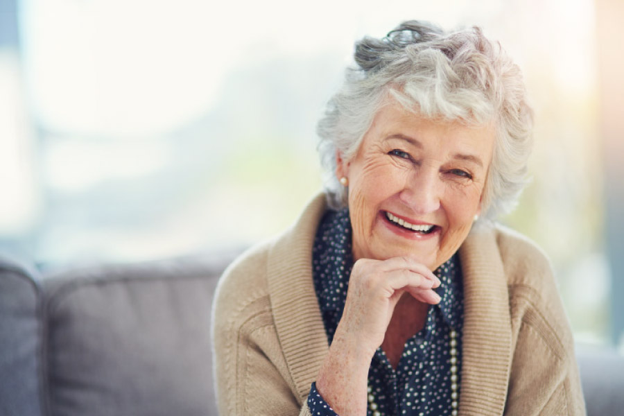 Smiling white haired elderly woman in a tan sweater resting her chin on her hand