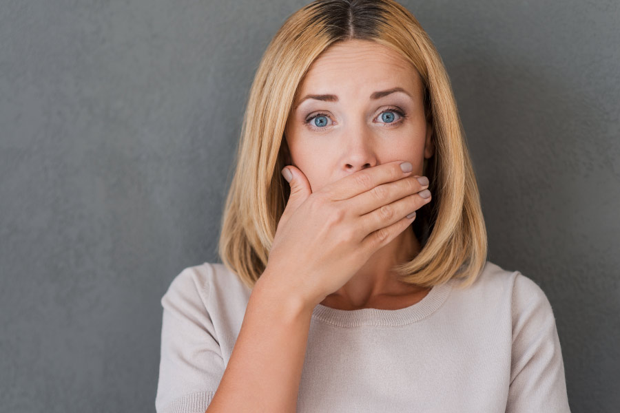 Blonde woman covers her mouth due to fear of bad breath or halitosis.