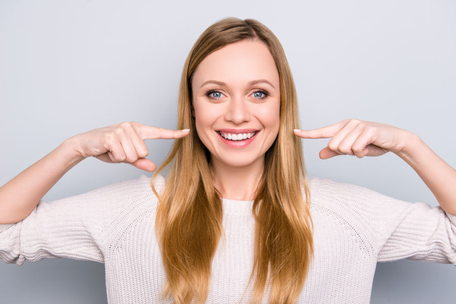 Smiling woman pointing to her white teeth.