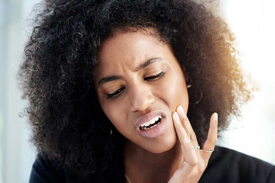 Dark haired woman has her hand to her cheek because of painful tooth sensitivity.