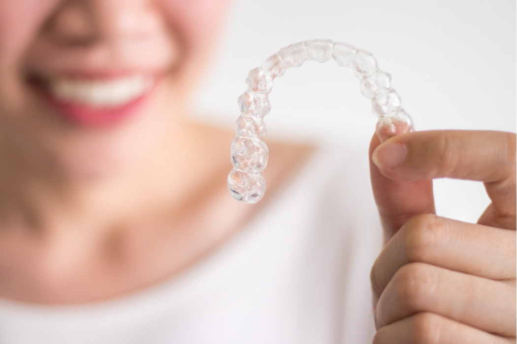 Blurry woman's face in the background holding a clear Invisalign aligner.